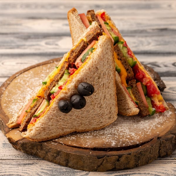 Two club sandwiches with ham, cheese, tomato, and cucumber, garnished with three black olives.