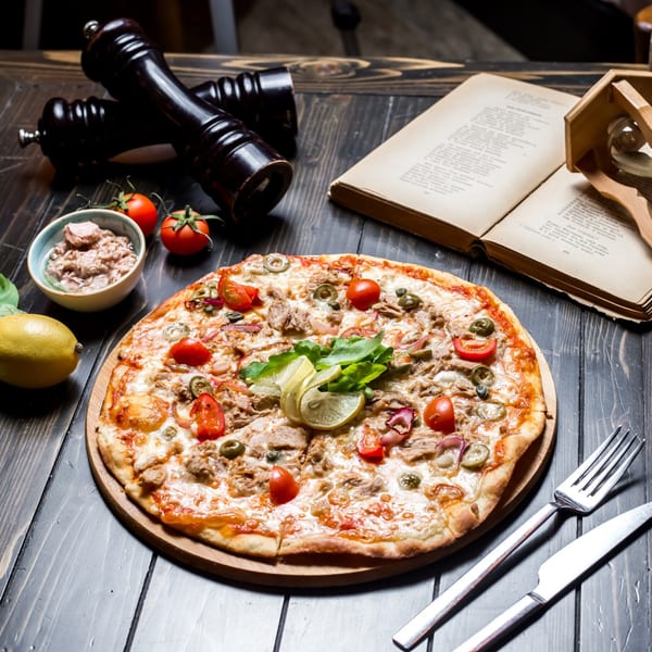 A Nutinis tuna pizza with cherry tomatoes, olives, and lemon slices on a wooden board.