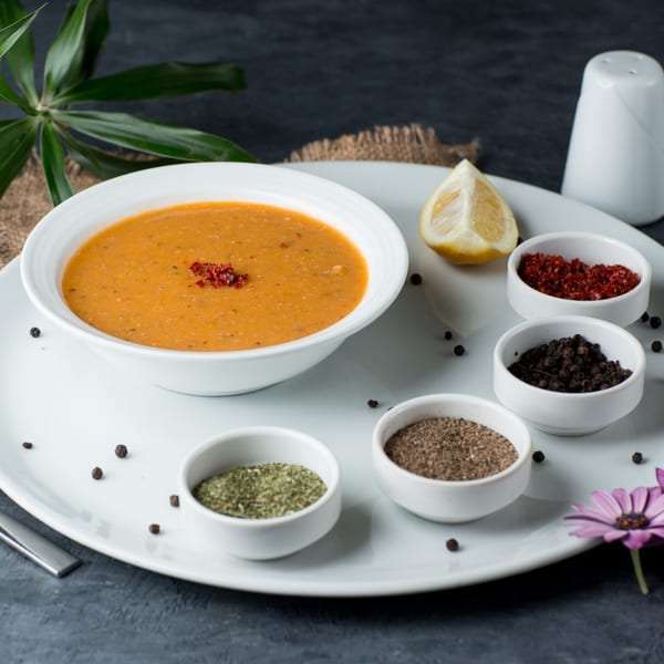 A bowl of Nutinis lentil soup with a lemon wedge and various spices on a white plate.
