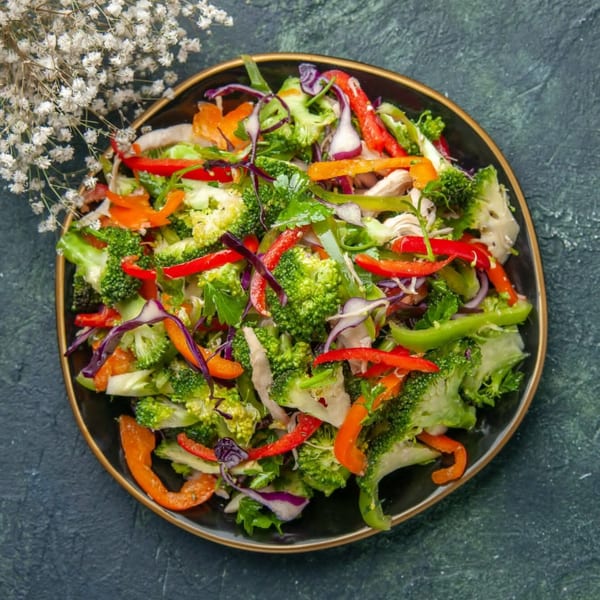 Nutinis' colorful salad with broccoli, bell peppers, red cabbage, and chicken on a dark plate.