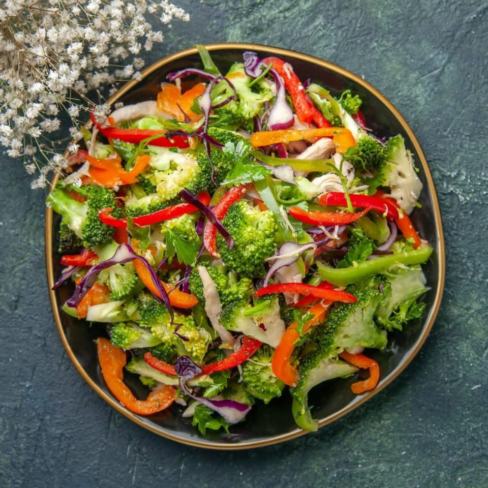 Nutinis' colorful salad with broccoli, bell peppers, red cabbage, and chicken on a dark plate.