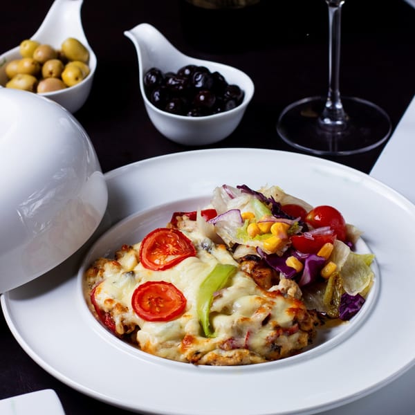 Nutinis' cheesy baked dish with sliced tomatoes and a side salad, accompanied by olives.