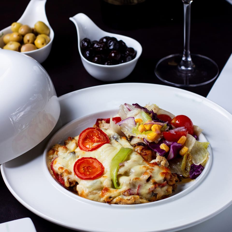 Nutinis' cheesy baked dish with sliced tomatoes and a side salad, accompanied by olives.