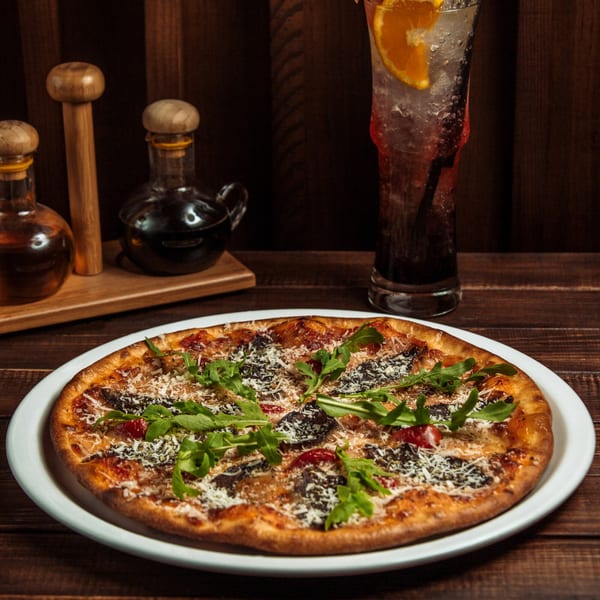 Nutinis pizza with arugula, mushrooms, and cheese, next to a drink and oil bottles.