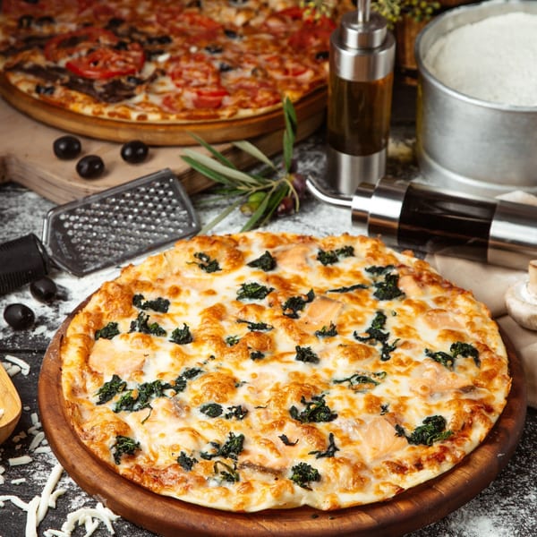 Nutinis' white pizza with spinach and chicken, with another pizza and ingredients in the background.